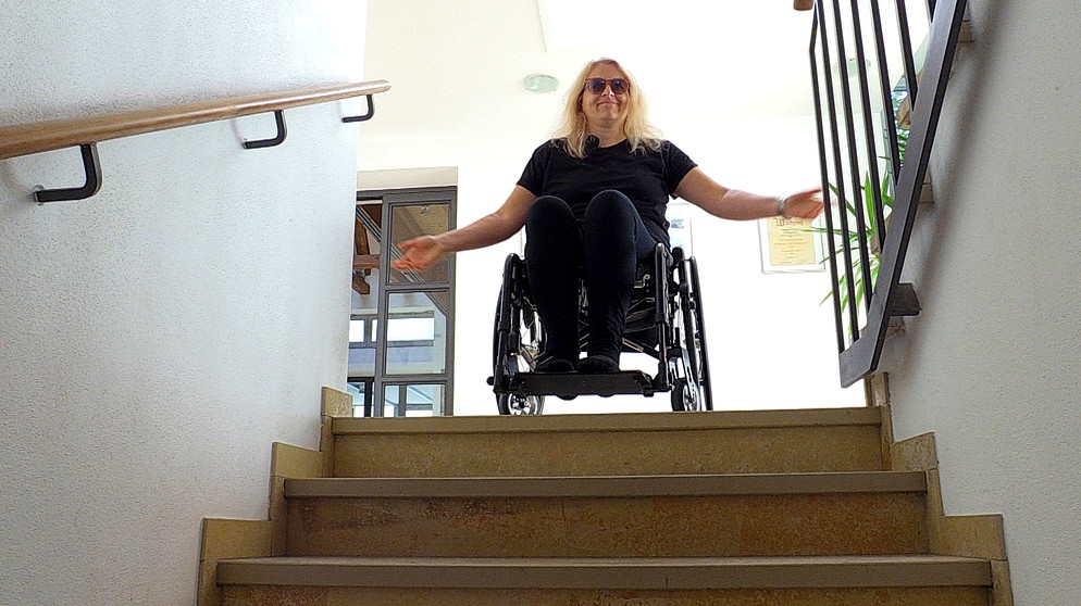 Kerstin Rathgeb im Rollstuhl. Unten wäre die Toilette: Eine Treppe aber versperrt für Kerstin Rathgeb, die im Rollstuhl sitzt, den Weg. | Bild: BR / Kontrovers | Judith Zacher