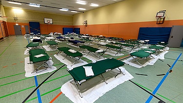 Feldbetten stehen in der Turnhalle von einem Gymnasium in der Nähe des Hauptbahnhofes. Die Stadt München hat in der Schule eine Notunterkunft für Flüchtlinge aus der Ukraine eingerichtet. | Bild: picture alliance/dpa | Sven Hoppe