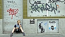 Einsamer Junge sitzt vor einem geschlossenen und mit Graffiti verschmierten Geschaeft. | Bild: picture-alliance/dpa