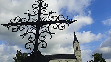 Ein Kreuz steht vor der Kirche St. Nikolaus in Garching an der Alz.  | Bild: picture alliance/dpa | Britta Schultejans