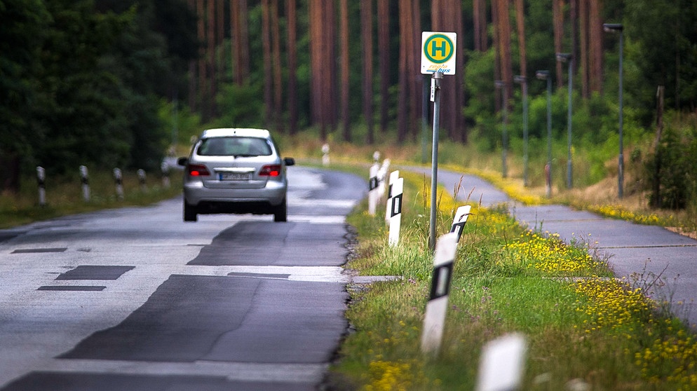 Auto fährt auf der Landstraße durch den Wald an einer leeren Bushaltestelle vorbei | Bild: picture alliance / photothek | Florian Gaertner
