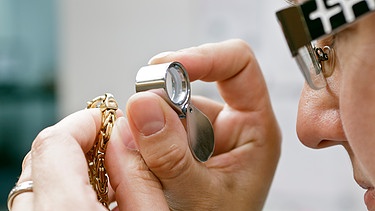 Eine Mitarbeiterin eines Pfandleihauses prüft mit einer Lupe eine Goldkette. | Bild: picture alliance / dpa Themendienst | Markus Scholz