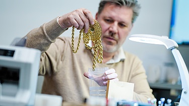 Pfandleiher steckt im Pfandleihhaus eine Goldkette in eine Tüte.  | Bild: picture alliance/dpa | Uwe Anspach