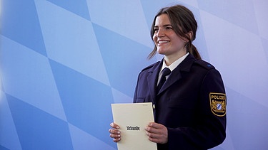 Die frischgebackene Polizeimeisterin Annelie freut sich über ihre Urkunde zum Ende ihrer Ausbildung.  | Bild: BR
