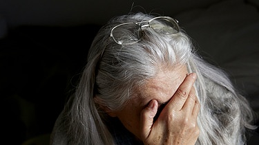 Verzweifelte ältere Frau hat die Hand vors Gesicht geschlagen | Bild: picture alliance/KEYSTONE | CHRISTOF SCHUERPF