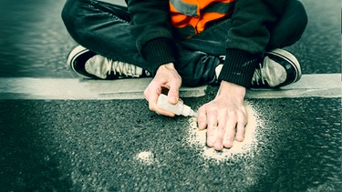 Ein Aktivist der Letzten Generation klebt sich die Hand mit Sekundenkleber auf der Straße fest. | Bild: picture alliance/SULUPRESS.DE; Bearbeitung: BR
