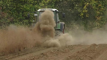 Ein Traktor fährt über ein Feld und wirbelt Staub auf | Bild: BR