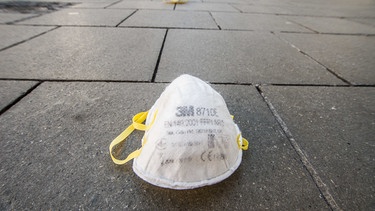 Atemschutzmaske auf einem Straßenpflaster | Bild: picture-alliance/dpa