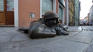 Kunstwerk auf der Straße: Mann aus Eisen, der aus Kanaldeckel klettert | Bild: BR