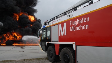Flammen mit schwarzem Qualm, im Vordergrund löschfahrzeug mit Aufschrift: Flughafen München | Bild: BR