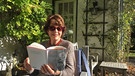 Marianne Koch liest ein Buch in ihrem Garten. | Bild: BR/Evelyn Schels