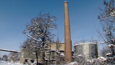 Eine aufgegebene Industrieanlage mit einem hohen Schornstein in verschneiter Landschaft | Bild: BR