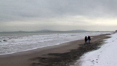 Zwei Spaziergänger an einem Strand | Bild: BR