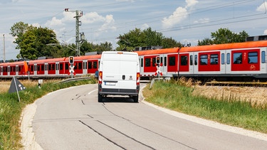 PKWs warten vor einer geschlossenen Bahnschranke, während die S-Bahn passiert. | Bild: BR/Herbert Ebner
