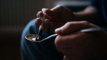 Ein Mann zieht Heroin in einer Spritze auf. | Bild: BR/Julia Müller