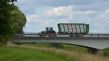 Traktor mit Anhänger überquert Brücke im Sommer zur Erntezeit. | Bild: stock.adobe.com/alissea