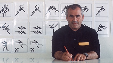 Aufnahme von 1970: Otl Aicher, Grafiker, Designer, Architekt, sitzt an seinem Schreibtisch. Im Hintergrund eine Tafel mit Piktogrammen, die er für die Sportarten der Olympischen Sommerspiele 1972 in München entworfen hat. | Bild: picture-alliance / Sven Simon