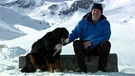 Unter unserem Himmel- Sanfter Tourismus in den Alpen: Thomi Blatter sitzt auf einem Baumstumpf im Schnee, nebem ihm sein Hund | Bild: BR