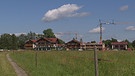 Unter unserem Himmel: Schwangau - Ein Dorf verändert sich: Eine grüne Wiese mit einem Weg, hinten stehen Häuser und Baukräne | Bild: BR