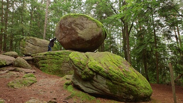 Mitten im Wald gibt es einen Wackelstein, der mit Muskelkraft zum Wippen gebracht werden kann. | Bild: BR