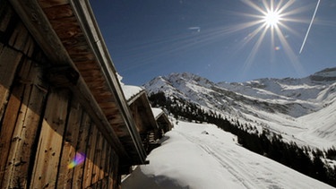 Unter unserem Himmel - Winter im Lechtal: Schneebedeckte Berglandschaft mit Holzhütten; die strahlende Sonne scheint am blauen Himmel | Bild: BR