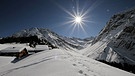 Unter unserem Himmel - Winter im Lechtal: Schneebedeckte Berglandschaft mit kleinen Holzhütten; die strahlende Sonne scheint am blauen Himmel | Bild: BR
