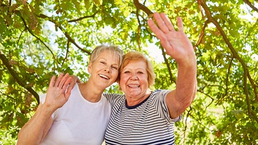 Zwei befreundete Seniorinnen winken glücklich beim Ausflug.  | Bild: picture alliance