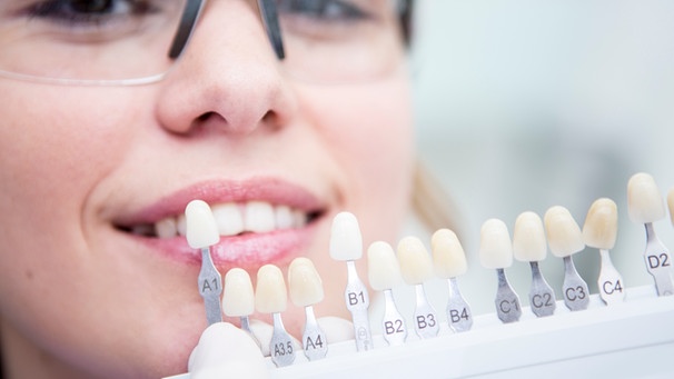 Frau beim Zahnarzt wählt Farbe für Zähne aus | Bild: Mauritius