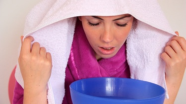 Eine Frau inhaliert, indem Sie ihren Kopf über eine Schüssel neigt und Dampf einatmet. Über ihrem Kopf hat sie ein Handtuch. | Bild: picture-alliance/dpa