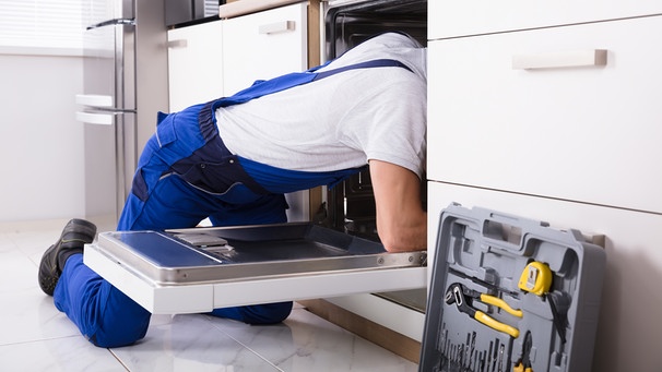 Ein Handwerker repariert eine Geschirrspülmaschine | Bild: BR/stock.adobe.com/Andrey Popov