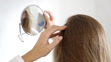 Symbolbild für schuppige Haare, Frau schaut in Spiegel, von hinten, lange Haare | Bild: BR / Britta Barchet