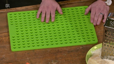 Eine grüne Backmatte mit vielen kleinen Herzförmchen auf einem braunen Tisch | Bild: Wir in Bayern