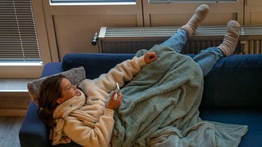 Eine junge Fraz wärmt ihre Füße an der Heizung | Bild: picture-alliance/dpa/Jochen Tack