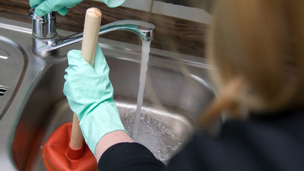 Frau reinigt verstopften Abfluss in einem Waschbecken. | Bild: picture alliance / dpa Themendienst