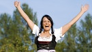 Junge fröhliche Frau im Dirndl reisst die Arme in die Höhe | Bild: picture alliance/Bildagentur-online