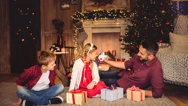 Es muss nicht alles perfekt sein! Familie in weihnachtlich geschmücktem Wohnzimmer mit Vater, Tochter, Sohn und Geschenken. | Bild: Colourbox