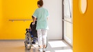 Eine Pflegerin schiebt eine Patientin im Rollstuhl | Bild: BR/stock.adobe.com/Reddragonfly