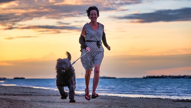 Hund läuft mit seinem Frauchen am Strand.  | Bild: picture alliance 