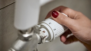 Frauenhand beim Einstellen des thermostatischen Heizkörperventils eines Heizkessels zu Hause | Bild: mauritius images / Westend61 / Zeljko Dangubic
