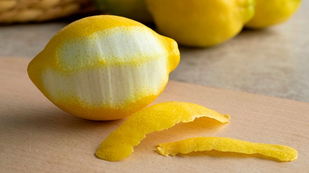 Eine teilweise geschälte Zitrone auf einem Holzbrett; neben der Zitrone liegen zwei Zitronenschalen und im Hintergrund sind Zitronen zu sehen. | Bild: mauritius images / Picture Partners / Alamy