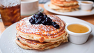 Drei Pancakes mit Heidelbeermus darauf auf einem weißen Teller; daneben ein kleines weißes Schälchen mit Ahornsirup | Bild: mauritius images / Luke Carre / Alamy / Alamy Stock Photos
