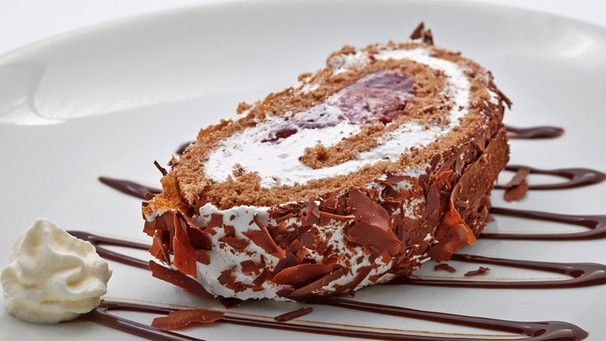 Eine Scheibe Schokoladenbiskuitroulade mit Sahne und Kirschen auf einem weißen Teller | Bild: mauritius images / foodcollection