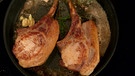 Zwei Schweinekoteletts werden mit Butter und Kräuter in einer Pfanne arosiert, das heißt übergossen. | Bild: Wir in Bayern