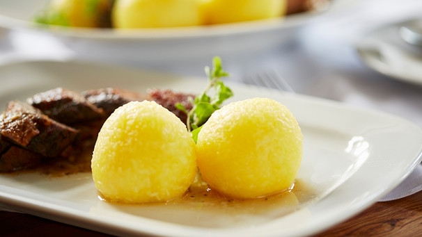 Zwei Kartoffelknödel mit gebratener Gans auf einem weißen Teller angerichtet | Bild: mauritius images / foodcollection