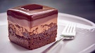 ein Stück Petit Four mit Schokolade auf einem kleinen Teller und einer Kuchengabel | Bild: mauritius images / foodcollection