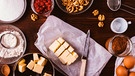Von oben fotorafiert: eine Schüssel mit Butter, eine Schüssel mit Kakaopulver, Mehl, Eier, Walnüsse, Zucker, Puderzucker auf einem braunen Tisch | Bild: mauritius images / Progressman / Alamy