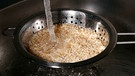 Brauner Reis wird in einem Sieb über einem Spülbecken gewaschen | Bild: Wir in Bayern