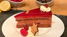 Ein Stück weihnachtlich dekorierte Schoko-Himbeer-Torte steht auf der "Wir in Bayern"-Küchentheke. | Bild: BR
