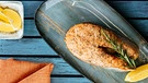 	Von oben fotografiert: ein gegrilltes Lachskotelett mit Kräutern und Zitrone auf einem blauen länglichen Teller auf einem blau lasierten Holztisch | Bild: mauritius images / foodcollection / kuzmin5d