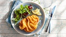 Von oben fotografiert: ein Wiener Schnitzel mit Zitronenscheiben und Salatgarnitur auf einem blauen Teller, der auf einem blau lasiertem Teller steht; | Bild: mauritius images / foodcollection / Frank Gölllner
